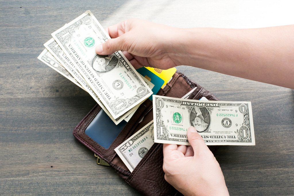 A wallet with dollar bills being held near it