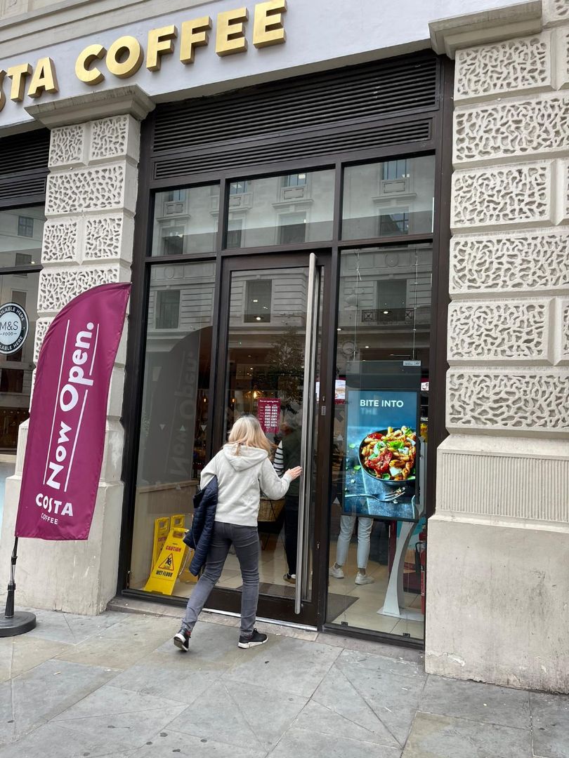 Woman entering Costa Coffee shop with LamasaTech high brightness double-sided window display in the window