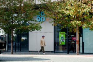 Man walking past a digital signage display in the window of a Co-op store.